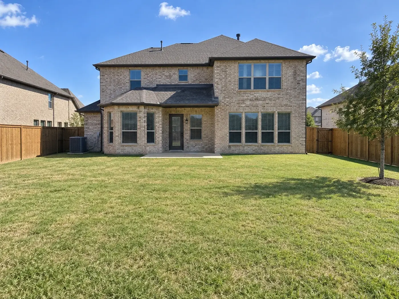A plain grass backyard behind a two-story Dallas–Fort Worth brick home before work began